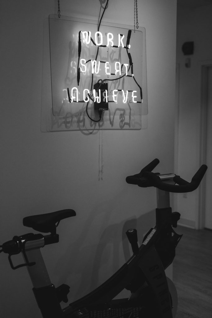 spin bike with neon sign that says "work, sweat, achieve"