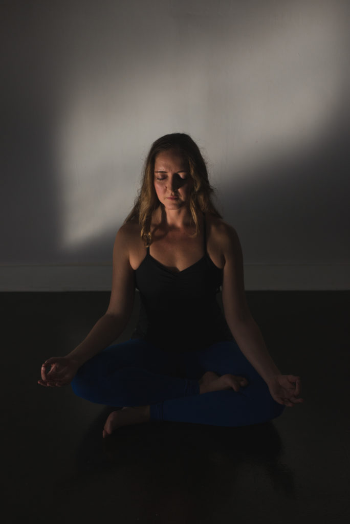 yoga teacher seated in a beam of sunlight meditating