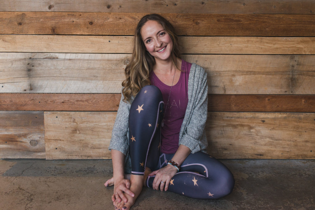 yoga teacher sitting against barn board wall smiling