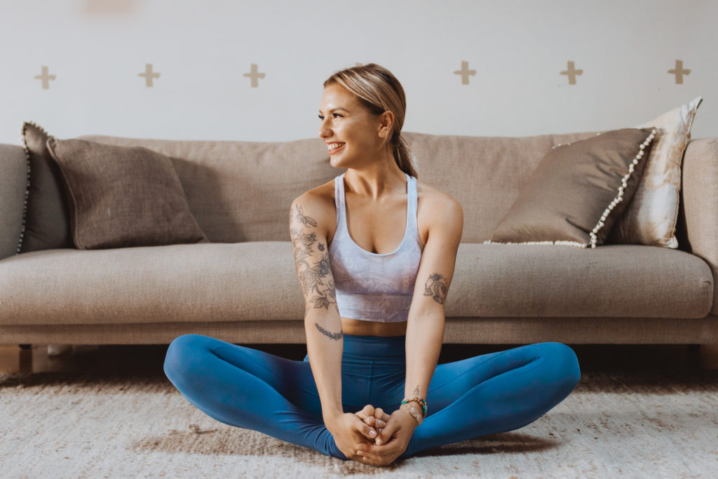 yoga teacher in sitting on the carpet in front of the couch in butterfly pose laughing