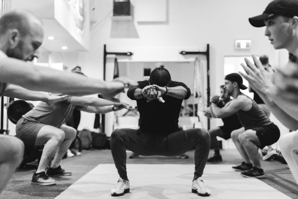 personal trainer demonstrating a squat surrounded by other men working out