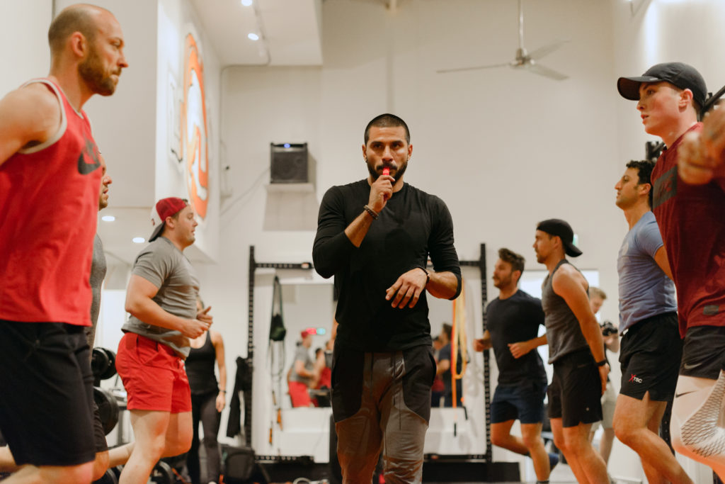 personal trainer blowing a whistle while men warm up