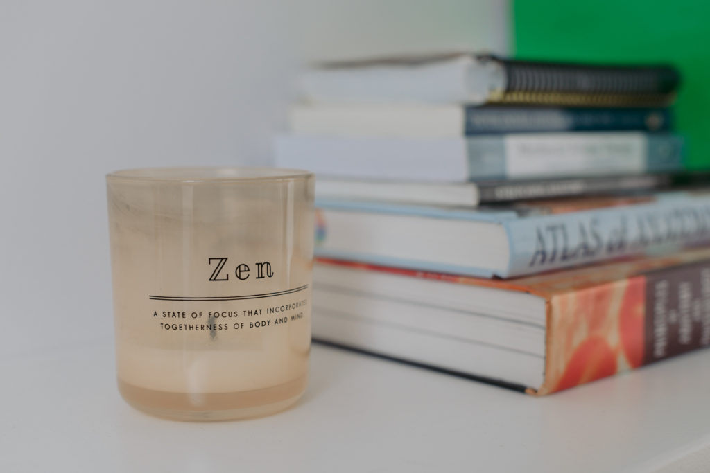 massage therapist scented candle with stack of books on bookshelf