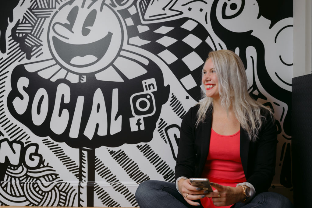 content marketer and social media expert sitting with her phone next to wall with social media icons