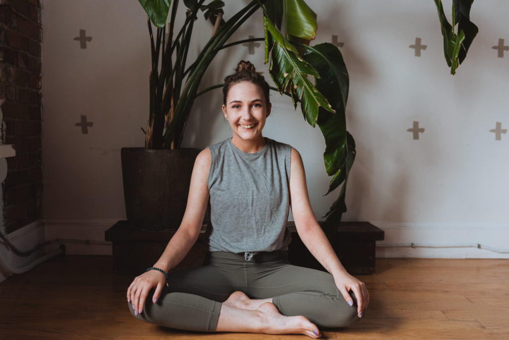 yoga teacher sitting cross legged in front of plant