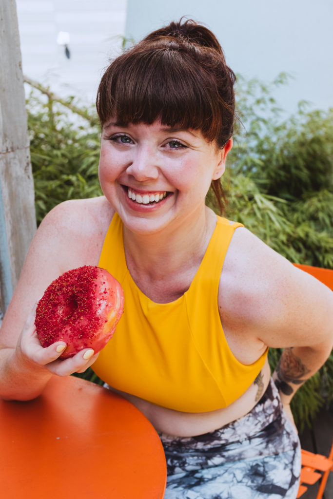 yoga teacher in bright yellow top holding pink donut