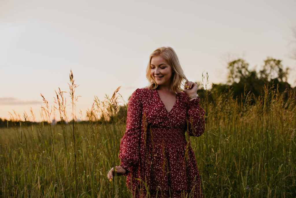 girl in a red dress in a field with long grass at sunset