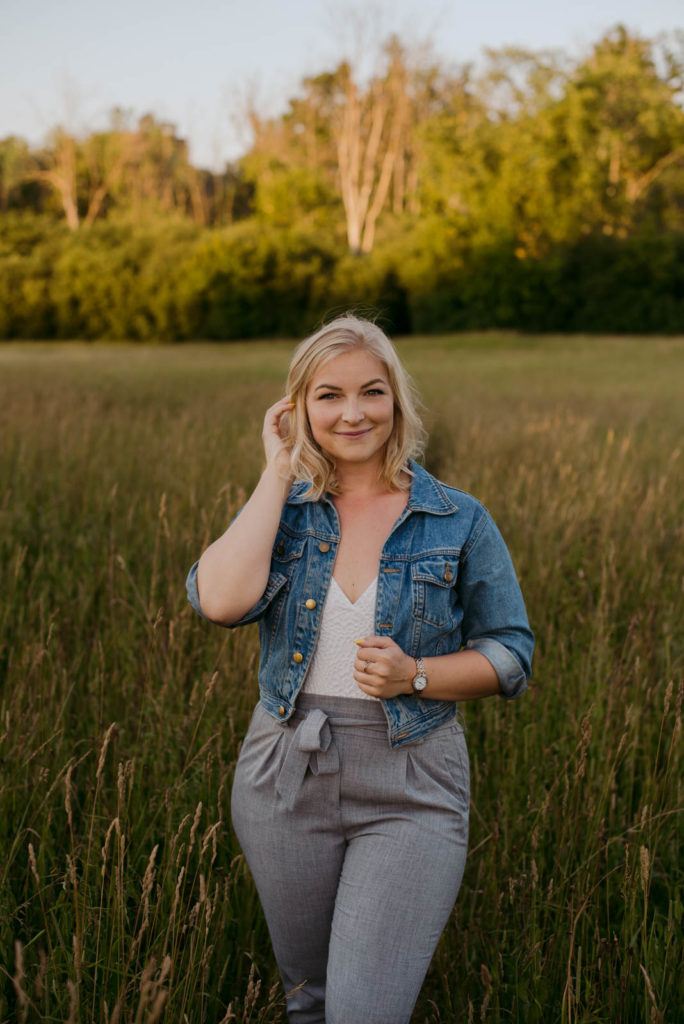 blonde girl in jean jacket standing in a field at sunset