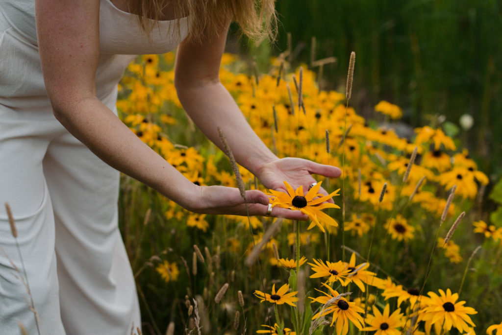 Stephanie Karlovits female entrepreneur holding a yellow daisy in a field of flowers