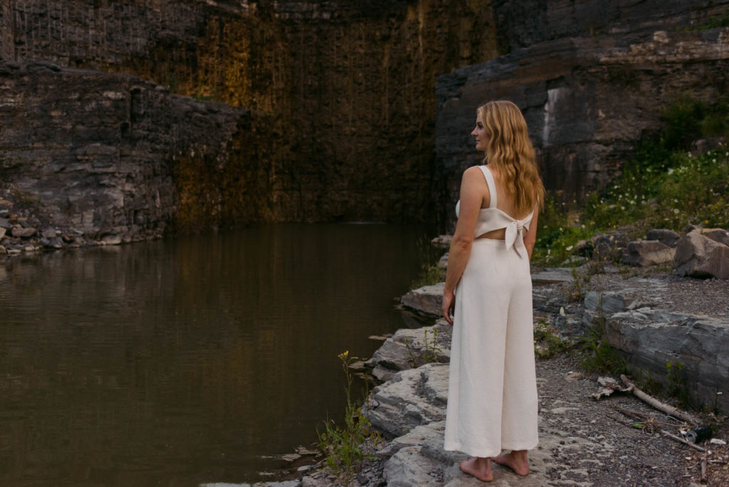 Stephanie Karlovits female entrepreneur wearing a white jumper standing on rocks by a dam