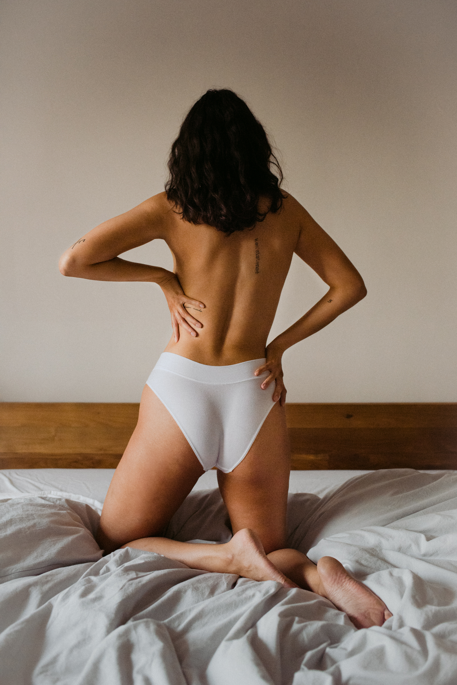 indie lingerie model on messy bed wearing only white bikini underwear