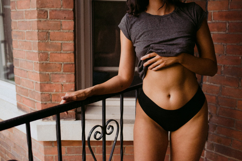 indie lingerie model standing on old brick balcony wearing black underwear