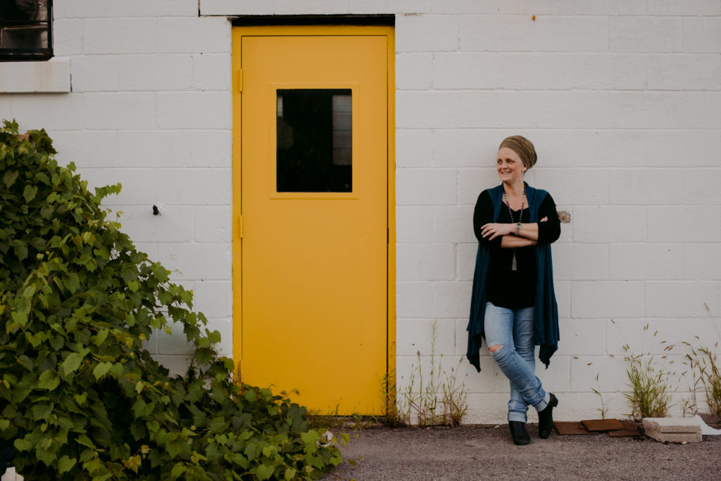 lifestyle photo of yoga teacher learning against a brick building next to a bright yellow door