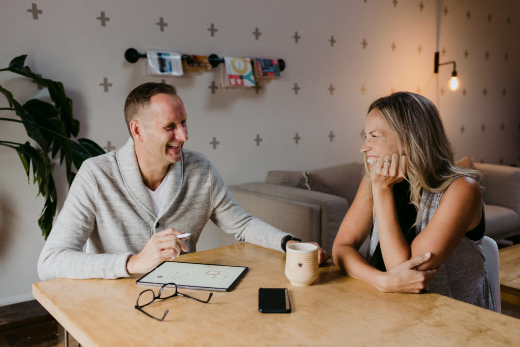 man and wife business owners laughing with each other sitting at a table working together