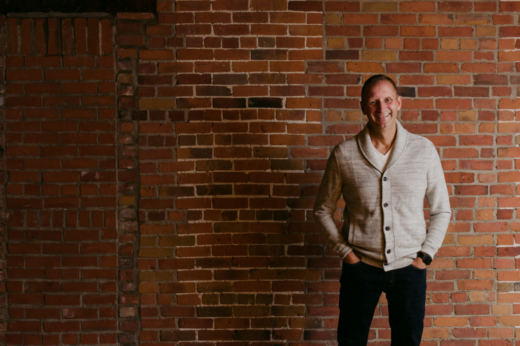 male business owner laughing standing against red brick wall