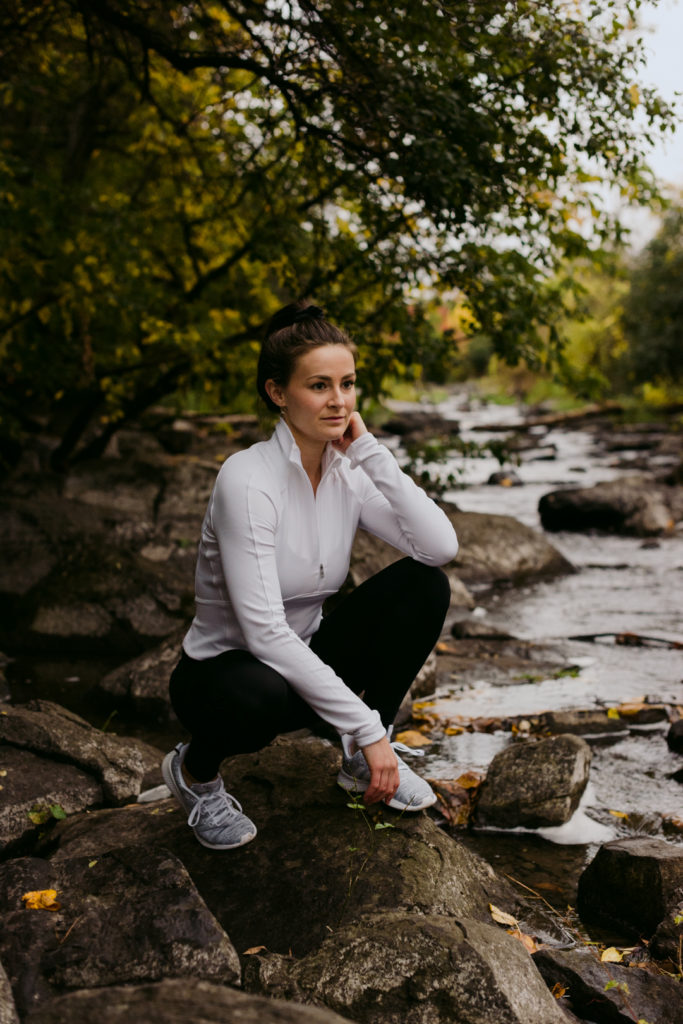 physiotherapist in lululemon apparel crouching on rocks by the water