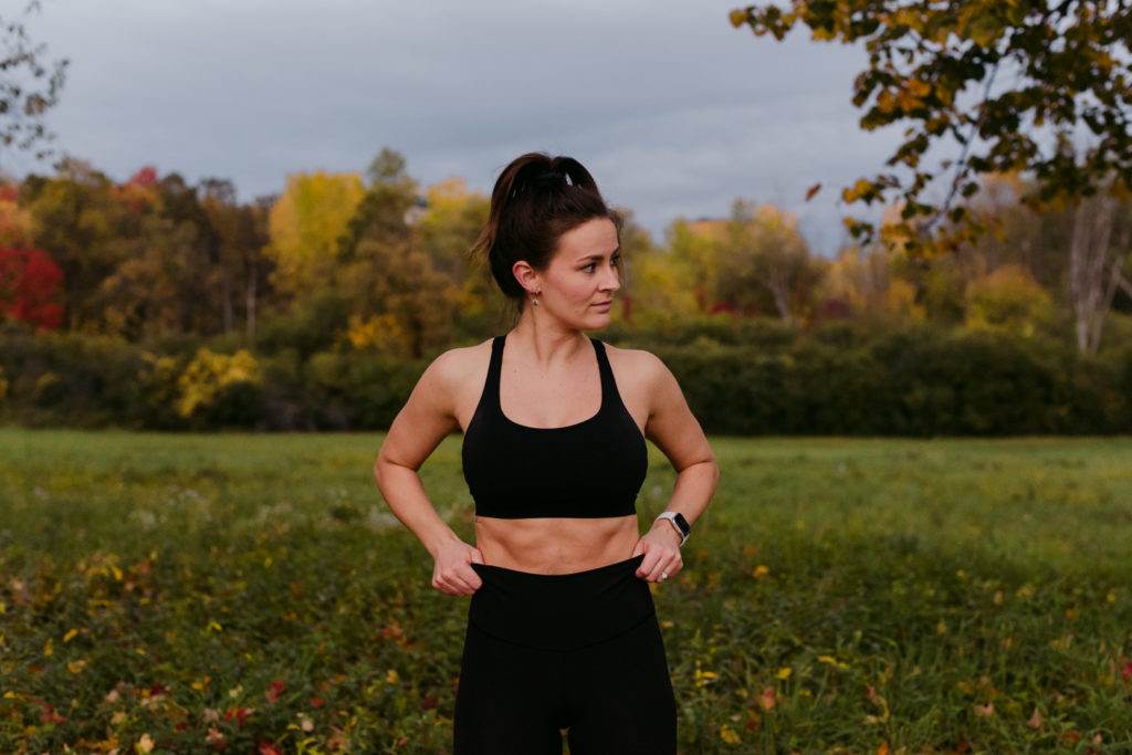 physiotherapist in lululemon pants and sports bra pulling up pants in a field during fall