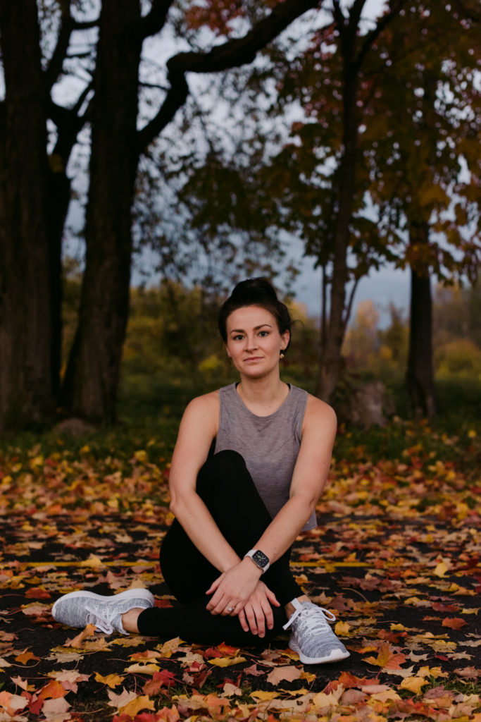 physiotherapist in lululemon apparel sitting on a path with fall leaves among the trees