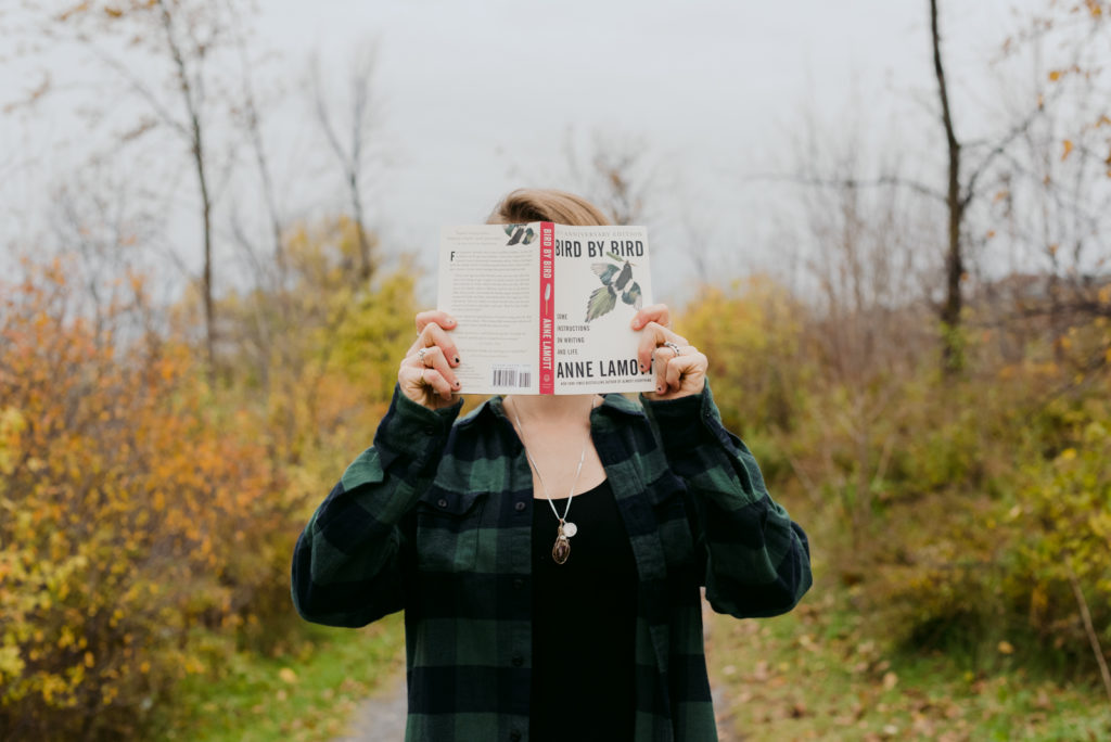 copywriter holding a book in front of her face standing on a path in the fall