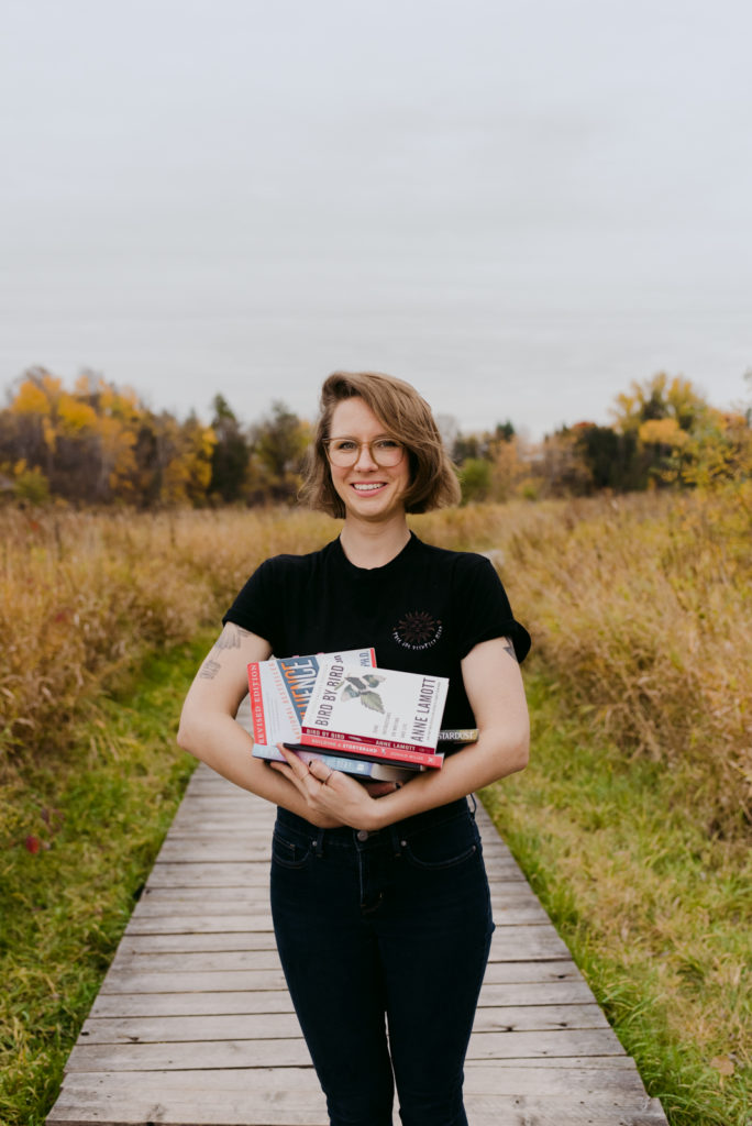 copywriter holding a stack of books standing on a boardwalk in the fall