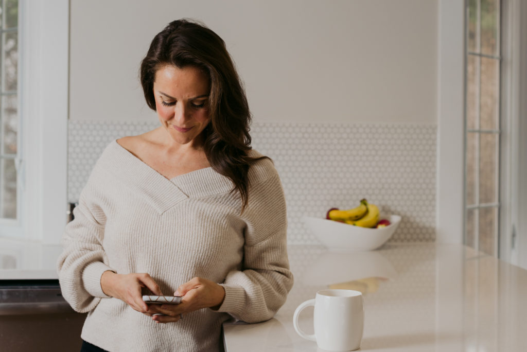 women wearing off the shoulder sweater holding cellphone drinking coffee