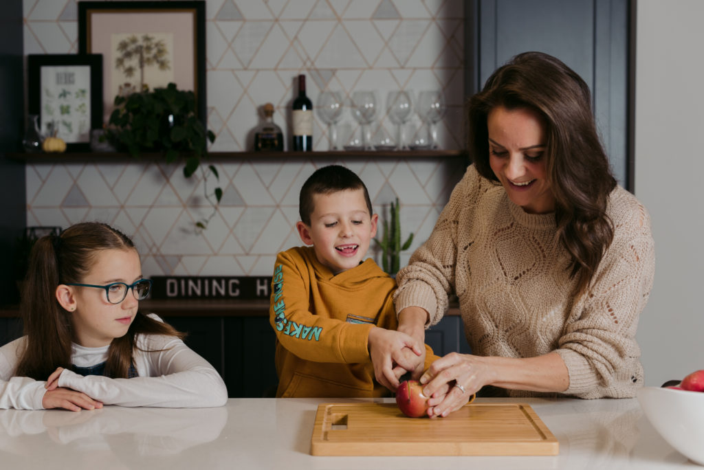 mom helping her kids cut up an apple at the kitchen counter