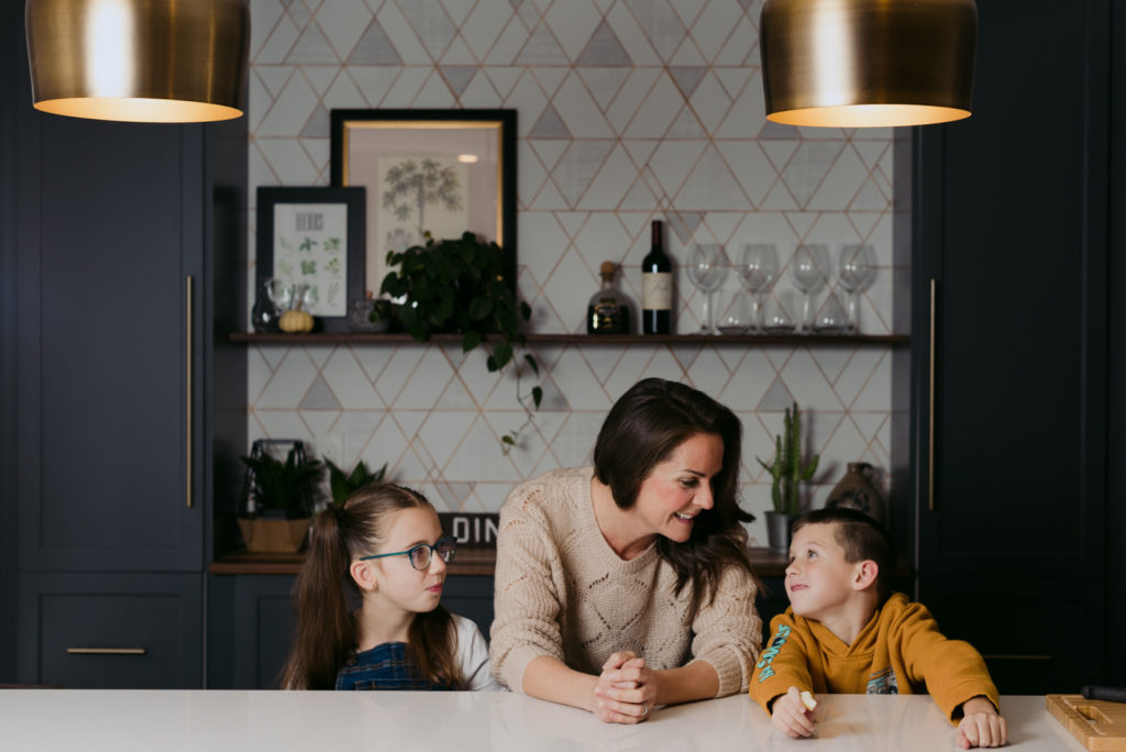 woman and her children sitting at the counter in the kitchen with wallpapered wall in the background