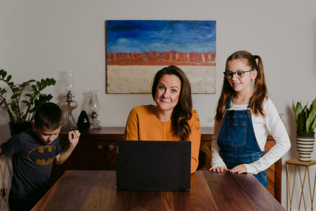 woman sitting at dining room table with her laptop and kids