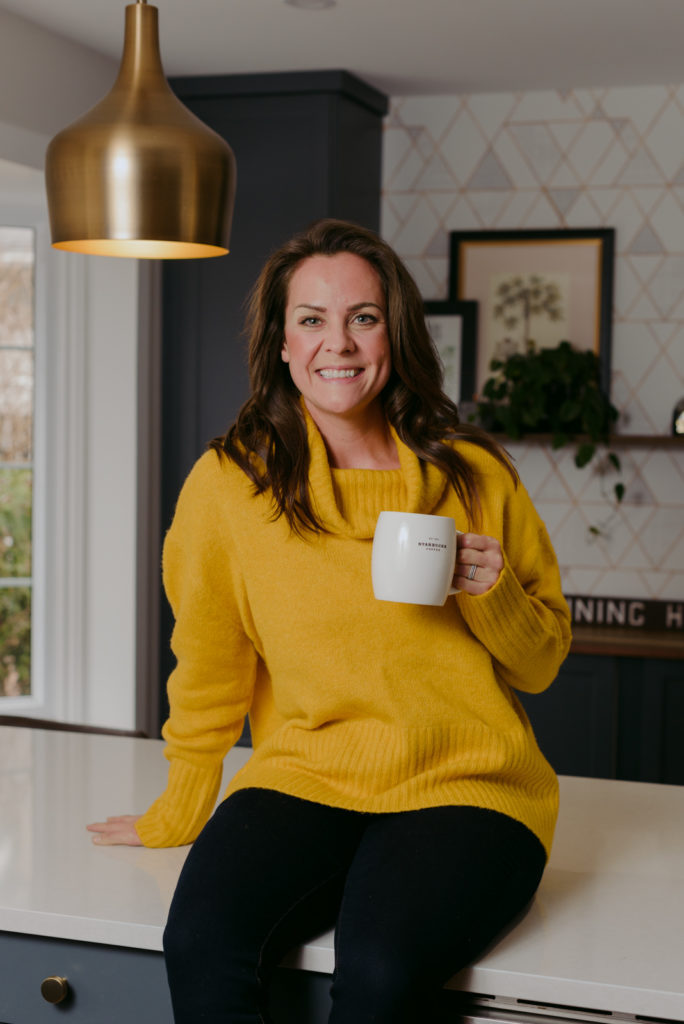 woman wearing yellow sweater sitting on the kitchen counter with coffee