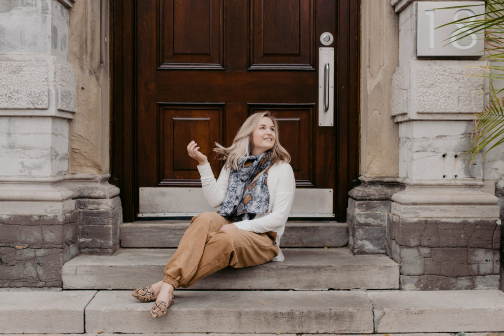 model sitting on steps outside big wooden door wearing corduroy pants