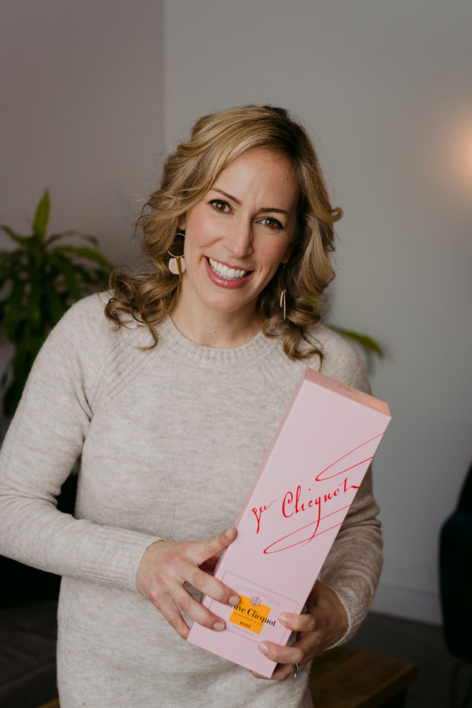 real estate agent Sarah Hunter holding bottle of Veuve Clicquot smiling at the camera