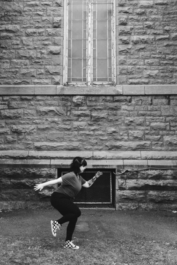 ottawa yoga teacher doing knee drive in front of stone church in black and white