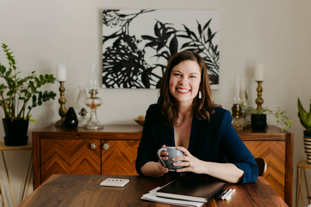 female entrepreneur sitting at a table with notebook and a coffee smiling at the camera