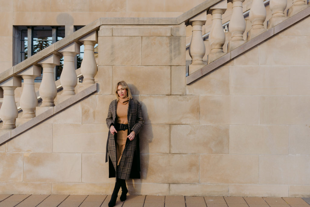 woman wearing plaid wool jacket leaning against stone steps by the Chateau Laurier
