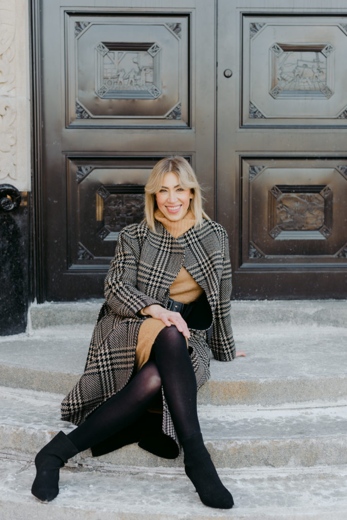 woman wearing plaid wool jacket sitting on steps in front of old metal door
