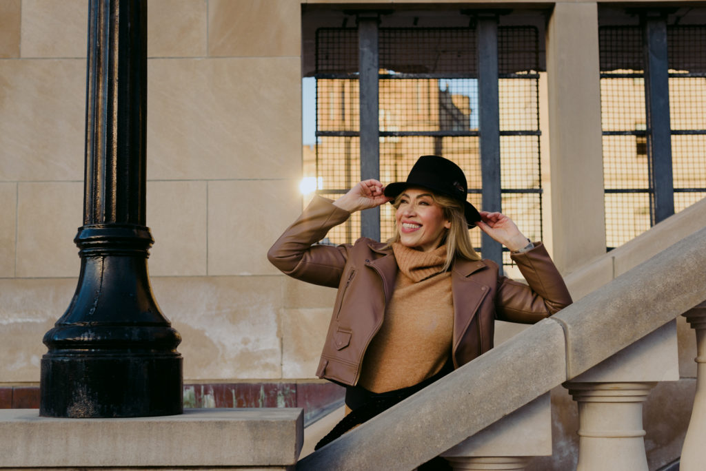 Woman wearing black hat on a stone staircase smiling into the sunlight