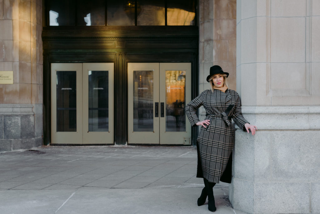 Woman wearing black hat and wool plaid coat in front of the Chateau Laurier in Ottawa