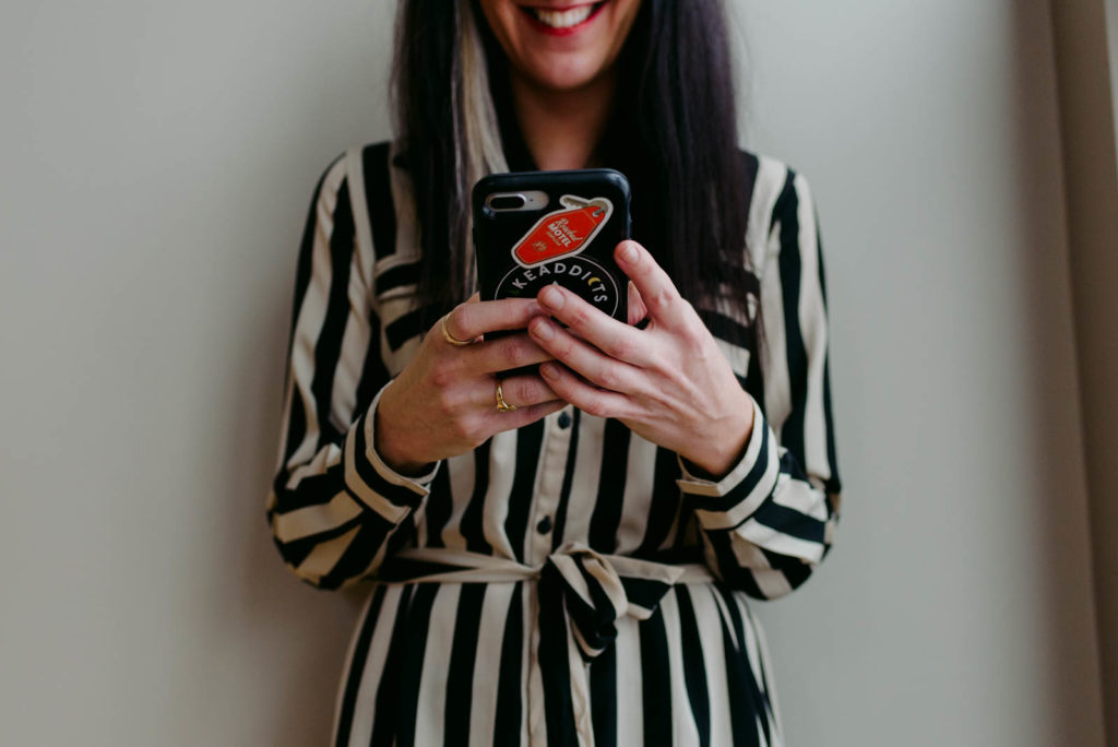 female entrepreneur holding her cellphone wearing a black and white striped dress