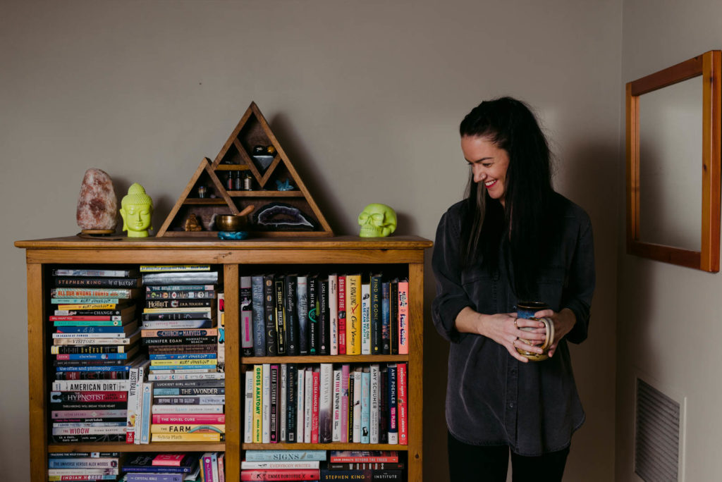 female entrepreneur standing next to a bookshelf with her coffee laughing