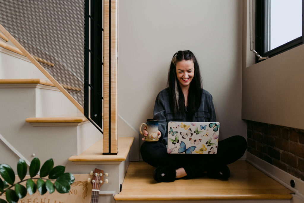 female entrepreneur sitting on a staircase with her coffee and laptop