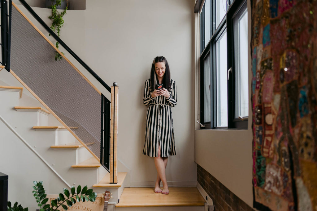 female entrepreneur standing on stairs wearing a black and white dress and holding her cellphone