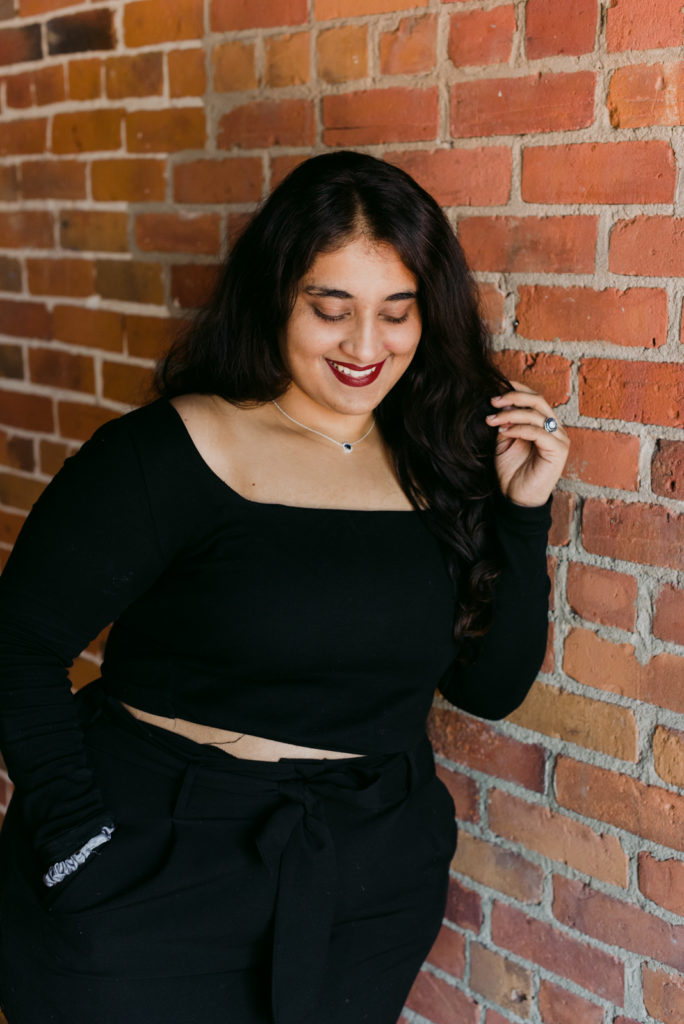 female entrepreneur wearing black leaning against a brick wall
