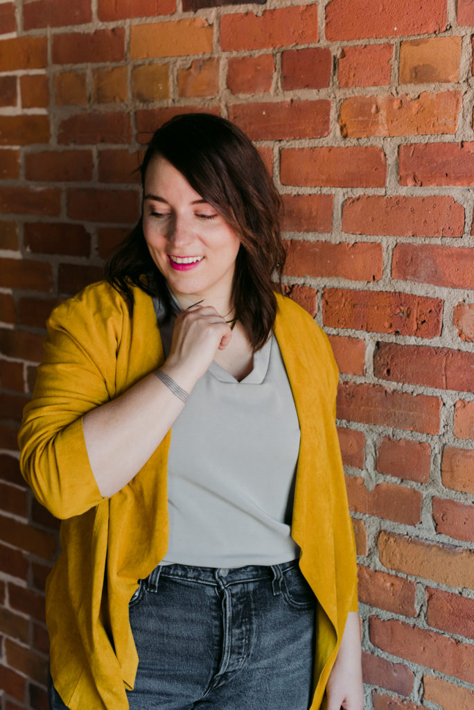 female entrepreneur wearing yellow leaning against a brick wall