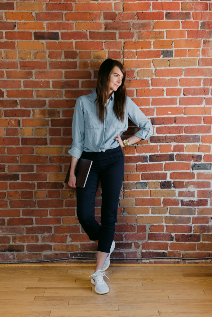 female entrepreneur holding laptop leaning against a brick wall