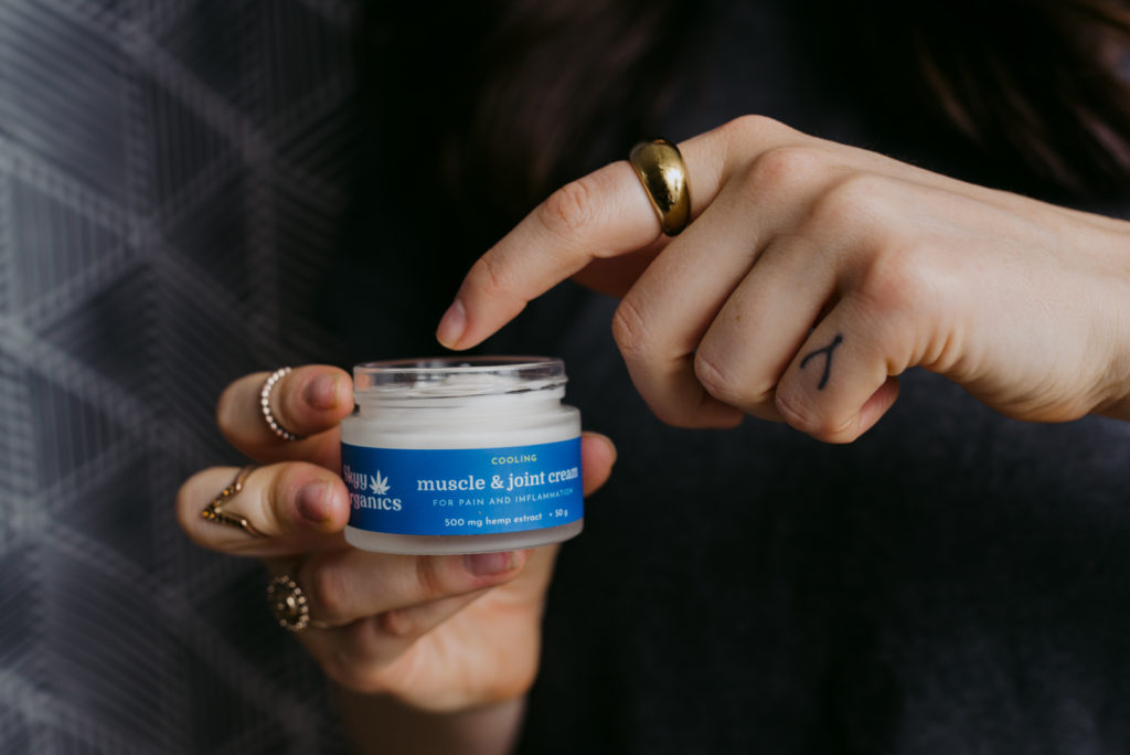 woman dipping finger into cbd muscle and joint cream container