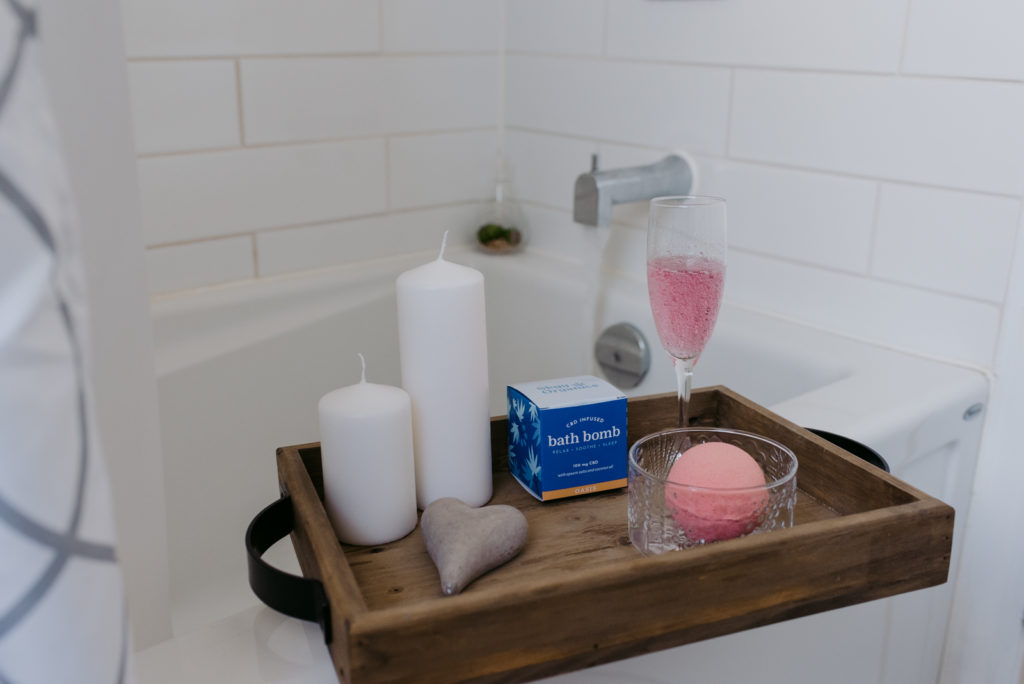 pink CBD infused bath bomb on wooden tray by the bathtub with rose in a champagne flute