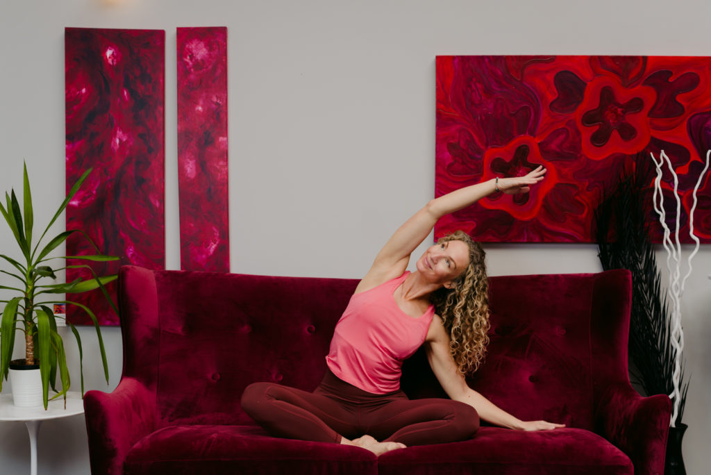 yoga teacher seated on a couch in a side bend pose
