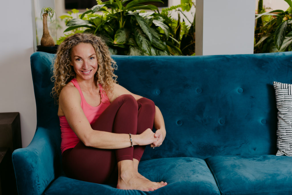 yoga teacher seated on a blue velvet couch smiling at the camera