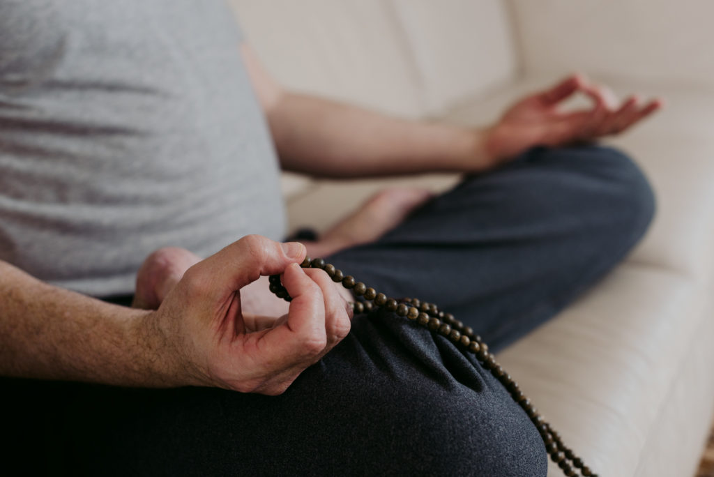 yoga teacher sitting on couch meditating with mala beads