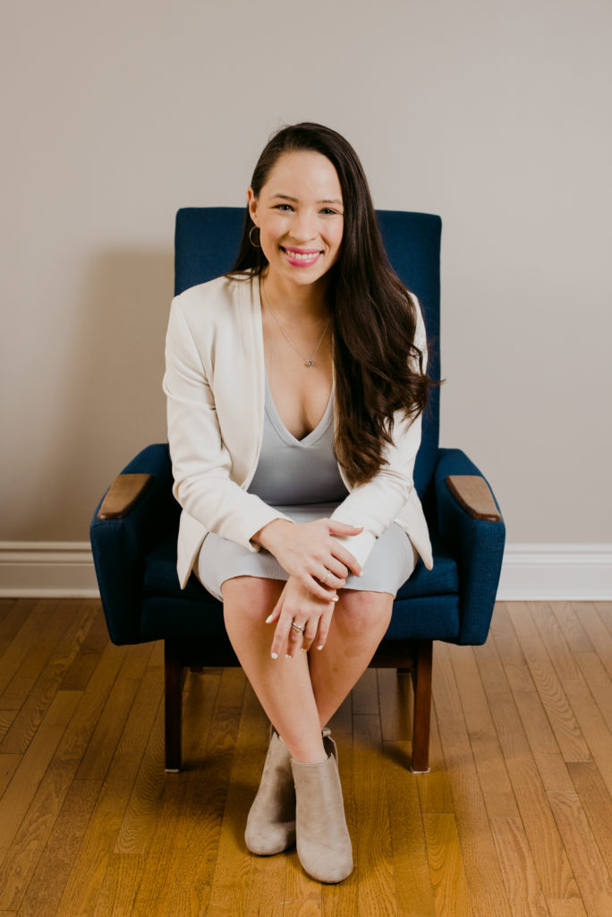 female real estate agent sitting in a blue chair leaning forward smiling at the camera